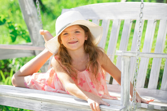 Child dreaming. Happy child girl laughing and swinging on a swing at the park in summer. Kids happiness and smile. Close up portrait of a beautiful child girl in hat dreaming. Dreamy kids face.