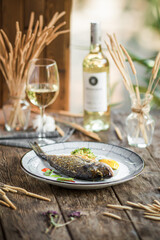 Plate of grilled gourmet fish with white wine on wooden background