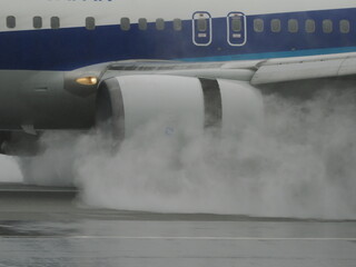 雨の日の滑走路に着陸した旅客機の逆噴射で巻き上がった水煙