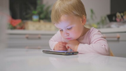 Cute Caucasian Baby Toddler Girl Watching Animated Movie Cartoon on Bright Screen Smartphone 
