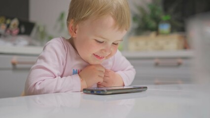 Cute Caucasian Baby Toddler Girl Watching Animated Movie Cartoon on Bright Screen Smartphone	
