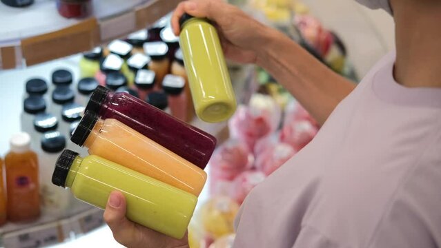 A woman customer in a store chooses bottles of freshly squeezed juice from different fruits and vegetables. Juice in plastic bottles of different colors, filled with vitamins from plants.