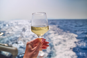hand with glass of white wine with sea or ocean on background - obrazy, fototapety, plakaty