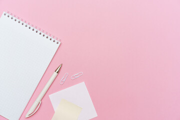 Workspace concept for school or office. Flat lay with an open notebook on a spring, a white color pencil, a plastic clip on paper background colors pink with copy space.