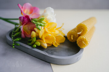 A candle lit on a gray tray. Bright freesia flowers.