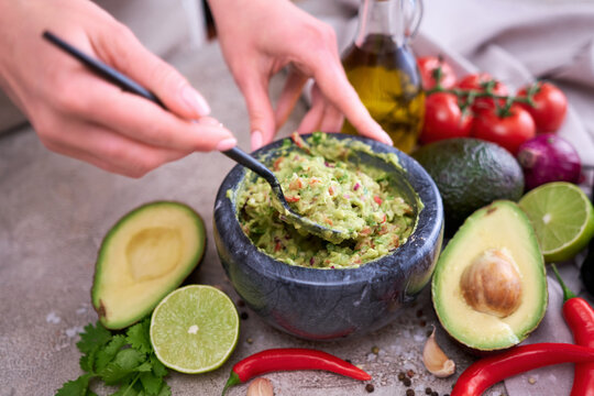 making guacamole - woman holding spoon with mixed minced ingredients