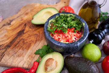 making guacamole - crushed avocado in marble mortar and ingredients