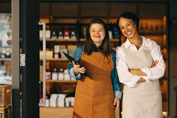 Two successful shop employees smiling at the camera happily - obrazy, fototapety, plakaty