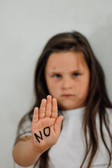  portrait of little bruised girl raising hand to cover mouth, showing inscription no on open palm. Protest against domestic violence, abuse, fighting, conflicts, bullying. Vertical.