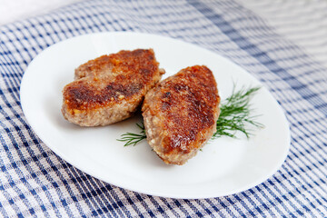 White plate with beef cutlets laying on traditional cheched kitchen towel