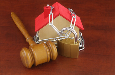 Law about real estate and court decision concept. Wooden judge gavel with chained house model.