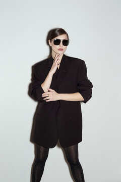 Trendy brunette woman dressed in a jacket is posing at studio wall background. Isolated portrait of modern caucasian girl.
