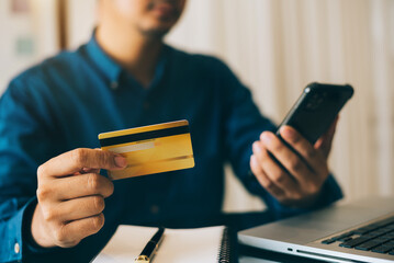 Male holding credit card and using smart phones.Businessmen working at home. Online shopping, e-commerce, internet banking, spending money, working from home concept.