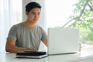 Smiling handsome asian man sitting on floor in living room and using laptop computer..