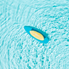 Fototapeta na wymiar Blue surfboard and a slice of lemon on the water. Minimal creative summer concept. Surfing, swimming and refreshing inspiration.