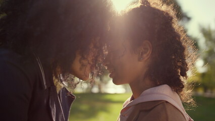 Loving mother touching noses with dreamy curly daughter golden sunlight closeup
