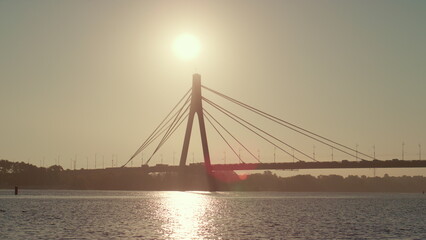 River bridge silhouette at clear sky summer day. Water reflect golden sunlight 