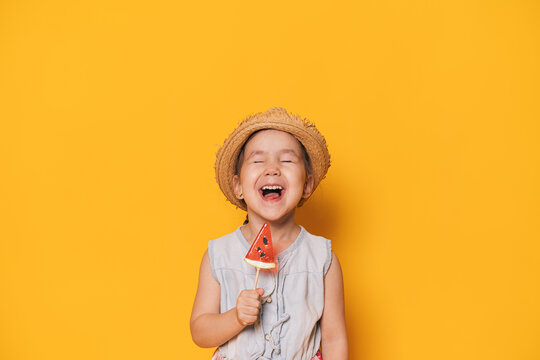 Laughing girl holding watermelon shaped lollipop against yellow background.