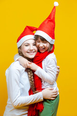 Family of Two Positive Caucasian Girls Sisters  In Festive Santa Hats Having Fun While Embracing And Toching by Cheeks On Yellow Background.