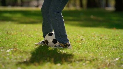 Closeup legs kicking football ball on green field. Summer active weekend in park