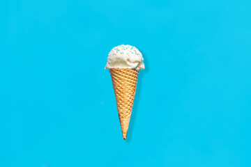 food, dessert and eating concept - close up of vanilla ice cream in waffle cone with sprinkles over blue background