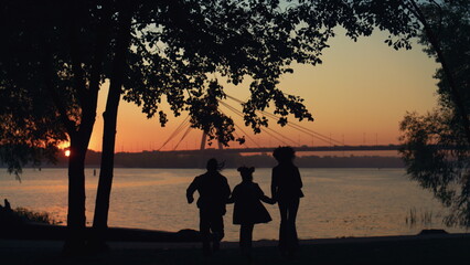 Fototapeta na wymiar Happy family silhouette run to river hold hands. Beautiful bridge waterway view.