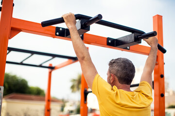 Street fitness, sport, exercising, training and lifestyle concept - man doing pulls up on horizontal bar outdoors