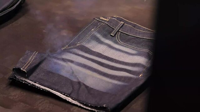 Jeans Shorts Being Distressed With Lasers In Factory. Close Up View With Smoke Rising
