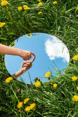 nature concept - hand touching sky reflection in round mirror on summer field