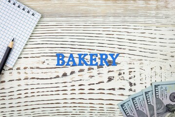 BAKERY - word (text) and dollars on a white wooden table, notebook, notepad. Business concept: buying, selling, commerce (copy space).
