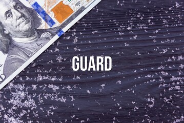 GUARD - word (text) on a dark wooden background, money, dollars and snow. Business concept (copy space).