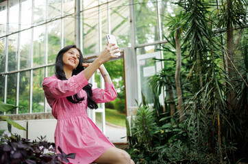 Portrait of a young beautiful woman with long wavy hair brunette communicates via video link in a tropical garden. Concept of new technologies for better life, travel, remote work