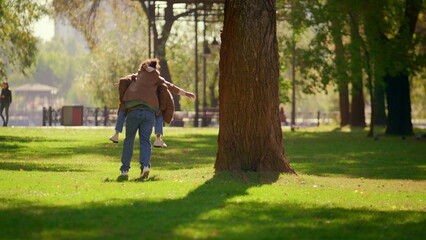 Naklejka premium Happy parent piggybacking daughter in sunny spring park. Loving father weekend.