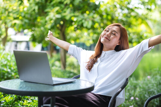 Portrait image of a woman with opened arms, stretching hands and relaxing while working on laptop computer in the park