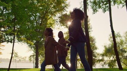 Child walking holding parents hands in green park. Happy family time outdoors