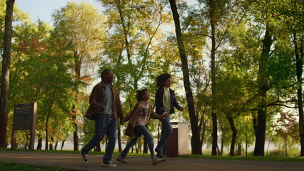 Fototapeta premium African american family walk autumn park together. Happy kid hold parents hands.