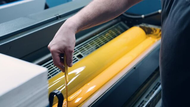 A worker in a printing house applies yellow ink to a packaging printing machine.
