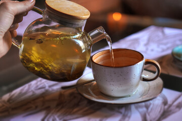 Grey cup with teapot. The hand holding the teapot pours herbal tea into a pot on saucer in soft...