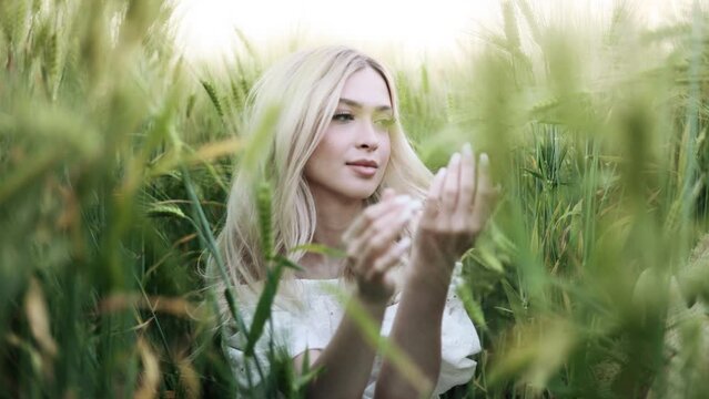 Portrait of gorgeous young woman sitting in green wheat field at the sunset. Concept of freedom.