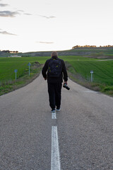 Photographer in nature walks down the center of a road towards the horizon