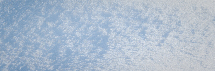 Beautiful winter background with snowy ground. Natural snow texture. Wind sculpted patterns on snow surface. Wide panoramic texture for background and design.