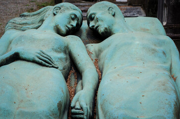 Fototapeta na wymiar Due amanti di bronzo riposano mano nella mano su una tomba del cimitero monumentale di Milano