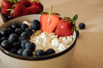 Curd with fresh blueberries and strawberries in a plate on a beige background. Healthy breakfast, front view, close up