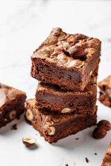 Stack of delicious brownie pieces with hazelnuts on marble background, close up