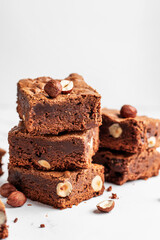 Stack of delicious brownie pieces with hazelnuts on marble background with copy space, close up