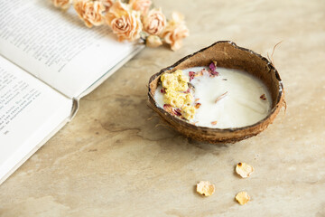 Handmade candle from soy and coconut wax in glass with wooden wick and dry flowers isolated on pastel beige background. Flat lay, top view, copy space