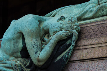 La statua di bronzo ossidato di un uomo sofferente che piange vegliando una tomba del cimitero...