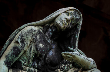 Il volto di bronzo ossidato di una donna sofferente sopra una tomba del cimitero monumentale di Milano