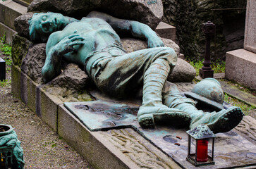 La statua di bronzo ossidato di un soldato morto che giace su una tomba del cimitero monumentale di...