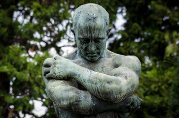 La statua di bronzo ossidato di un uomo sofferente sopra una tomba del cimitero monumentale di...